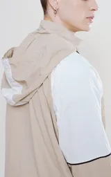 Anorak unisex beige y blanco con capucha, cierre parcial con cremallera, bolsillo tipo canguro con solapa y cordones ajustables con texto en la capucha.