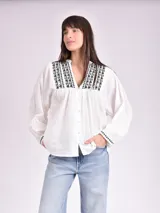 Camisa blanca de manga larga con bordado negro en el cuello y puños, con botones frontales.