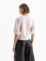 Top negro de largo a la primera cadera con mangas bombachas que incorporan flecos, aportando movimiento y textura al diseño. Confeccionado en una mezcla de hilados que combinan suavidad y estructura.