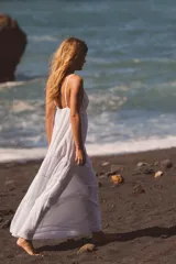 Vestido midi de color blanco confeccionado en gasa de algodón. Presenta escote en pico, tirantes finos ajustables y detalles de bordados a tono. La falda tiene un diseño escalonado con volados y cuenta con forro interior.