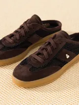 Zapatilla mule color marrón de cuero vacuno descarne combinado con rafia en los laterales. Lleva cordones al tono y detalle de aplique Cherry.