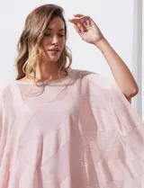 Poncho blanco de tejido calado con lurex, terminación asimétrica y cuello redondo.