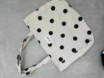 Bolso tipo tote bag de lona color crudo con estampado de lunares negros. Posee dos asas de hombro y una etiqueta blanca con el logo "AIRE" en el centro.