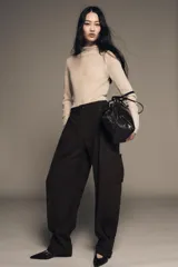 Pantalón cargo de algodón color marrón oscuro, tiro medio, con pliegues frontales, bolsillos delanteros ocultos y bolsillos de plastrón con solapa y botones a presión en las piernas. El bajo del pantalón tiene una trabilla con botón y se muestra doblado hacia afuera.