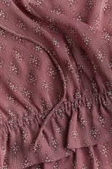 Blusa rosa con estampado floral, cuello con volados y escote en V con tiras finas para atar. Modelo de manga larga con hombros caídos y fruncido elástico con ribete de volados en puños y bajo.