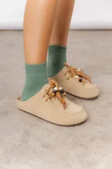 Zueco de cuero gamuzado color beige, con cordones decorativos con cuentas y piezas envueltas en cuero. Tiene plantilla acolchada y base liviana.