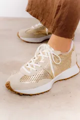 Zapatillas deportivas color beige con detalles metalizados dorados, confeccionadas en cuero con perforaciones, cordones ajustables y suela de goma dentada.
