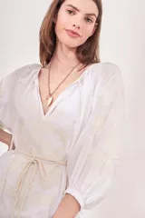 Vestido túnica largo color blanco, con escote en V, mangas 3/4 y bordado floral en el frente y las mangas. Incluye lazo de ajuste en la cintura con borlas.