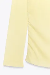 Camiseta negra de algodón con escote recto, hombros descubiertos y mangas largas. Presenta detalle de frunces en el frente.
