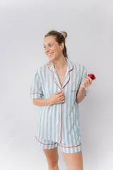 Pijama de lino a rayas verticales blancas y celestes, con vivos rojos. Incluye camisa de manga corta abotonada y short con elástico en la cintura.