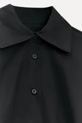 Camisa negra oversize de popelina de algodón, con cuello solapa, manga larga con puños abotonados, pinzas en la espalda y cierre frontal con botones.
