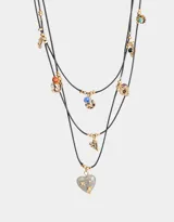 Collar corto de cordón negro con múltiples dijes dorados y piedra en forma de corazón.