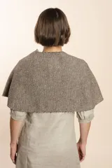 Chal asimétrico de lana color gris claro, con cortes en los hombros y doble ojal de fieltro para mantener el cruce. Terminación pespunteada y al corte.