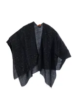 Capa o poncho de tejido de punto negro con patrón de zigzag y detalles brillantes o lentejuelas incrustadas. Presenta un escote en V cruzado y bordes deshilachados.