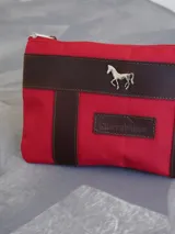 Sobre tipo cartuchera color borgoña, de lona con terminaciones en cuero marrón. Tiene cierre superior y aplique de cuero con el logo de la marca.