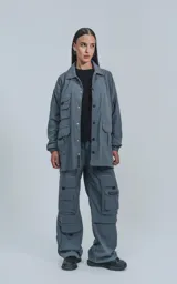 Campera gris con broches en el delantero, forrada con red, múltiples bolsillos con detalles en réflex y puños elásticos en las mangas. Confeccionada en textil liviano 100% poliéster y calce oversize.