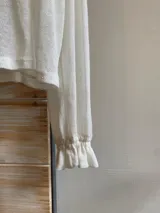 Blusa color marrón claro confeccionada en lino, de manga larga con elástico en los puños, escote en V con doble lazo y corte irregular.