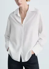 Camisa blanca de lyocell con cuello camisero, corte recto, cierre frontal con botones, mangas largas y puños abotonados.
