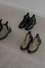 Botines Chelsea de cuero color verde oliva y negro, con elásticos laterales negros, tirador trasero y suela track de goma color verde oliva.