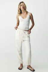 Pantalón jogger color gris claro, de tiro alto con cintura elástica ajustable con cordones, bolsillos delanteros y traseros con solapa, y puños elásticos en los tobillos.