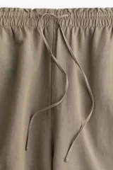 Pantalón de corte holgado color arena, confeccionado en tejido liviano de mezcla de lino. Modelo de tiro alto con elástico revestido en la cintura, cordón para ajustar fino y piernas amplias con bolsillos al bies.