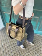 Cartera tipo tote bag de cuero color verde oliva, con doble asa corta de cuero marrón y correa larga extraíble y regulable de cuero marrón. Tiene un bolsillo frontal con cierre y un bolsillo interno.