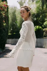 Top blanco de encaje con bordados florales, cuello redondo y mangas largas.