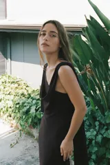 Vestido largo marrón con escote asimétrico y tirante ancho. Tiene una capa de tejido transparente a tono sobre el hombro y abertura lateral en el ruedo.
