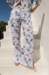 Pantalón de lino blanco con estampado floral azul, de tiro medio y corte semi-oxford con tajos en el ruedo.