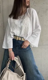 Blusa blanca de manga larga acampanada con bordado floral en el frente y cierre con botones.