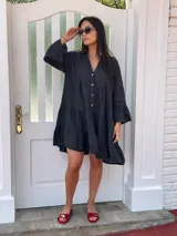 Vestido corto negro de lino, con escote en V, botones frontales y mangas largas acampanadas con volados.