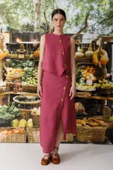 Conjunto de top sin mangas y falda midi color fucsia, con botones dorados. La falda presenta una abertura lateral.
