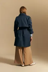 Trench color beige de corte clásico con cuello amplio, botones frontales, detalles en los hombros y mangas largas.