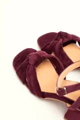 Sandalia de terciopelo verde con taco cuadrado de 7 cm, punta cuadrada y tiras anchas anudadas en el empeine. Cuenta con una tira fina ajustable al tobillo con hebilla dorada.