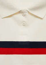 Polo crop color crema con cuello clásico, cierre de botones parcial y mangas cortas con dobladillo. Presenta una franja horizontal con rayas rojas y azul marino en el pecho.