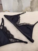 Conjunto de lencería negro, compuesto por un corpiño triangular de algodón con detalles de encaje y una tanga de algodón con detalles de encaje.