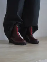 Botas de cuero color borgoña con suela track y cremallera frontal roja.