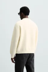 Jersey color crema de punto con textura, cuello redondo, manga larga y corte relaxed fit.