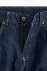 Pantalón jean de tiro alto, color azul oscuro, con corte holgado y pierna recta. Tiene cinco bolsillos y cierre con botón.