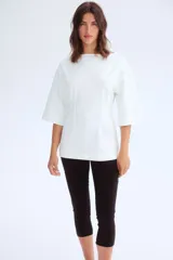 Remera larga color blanco de punto pesado de algodón, con escote barco, hombros caídos, mangas al codo y cintura entallada con pinzas acolchadas.