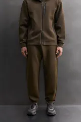 Pantalón jogger de entrenamiento, corte regular fit, color verde oliva oscuro. Confeccionado en tejido técnico compacto de algodón con elasticidad y efecto neopreno. Presenta cintura elástica ajustable con cordón blanco, bolsillos frontales y un bolsillo lateral con cierre de cremallera. El bajo termina en puño.