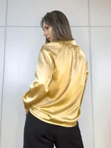 Camisa color dorado de satén plisado, con cuello clásico, cierre frontal con botones y mangas largas con puños abotonados.