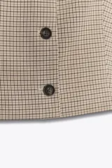 Chaleco marrón claro con estampado de cuadros, cuello redondo, sin mangas y cierre frontal con botones marrones.