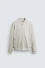 Cazadora bomber color gris claro, de corte regular fit y tejido efecto ante. Tiene cuello, puños y bajo de rib elástico, bolsillos de vivo en la cadera y cierre frontal con cremallera.