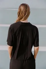 Camisa negra de manga corta con cuello solapa y escote pico. Detalle de nido de abeja en la espalda y cierre frontal con botones.