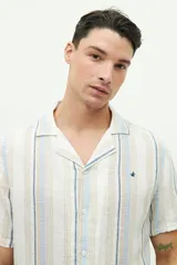 Camisa de manga corta confeccionada en lino y algodón a rayas verticales en tonos blanco, gris y beige. Tiene cuello tipo cubano, corte regular y logo bordado en el pecho.