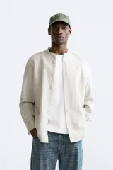 Camisa color beige claro, de corte relaxed fit, confeccionada en tejido de lino y algodón. Tiene cuello mao, manga larga con puños abotonados y cierre frontal con botones.