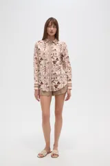 Camisa de manga larga con estampado de motivos playeros en tonos marrones sobre fondo beige, cuello camisero y cierre frontal con botones.