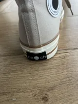 Zapatillas de lona blancas de caña alta con cordones y puntera de goma. Logo de durazno engomado en la base y en la cara interna.