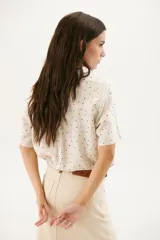 Camisa blanca con estampado de lunares negros, de corte clásico, manga corta y cuello camisero.